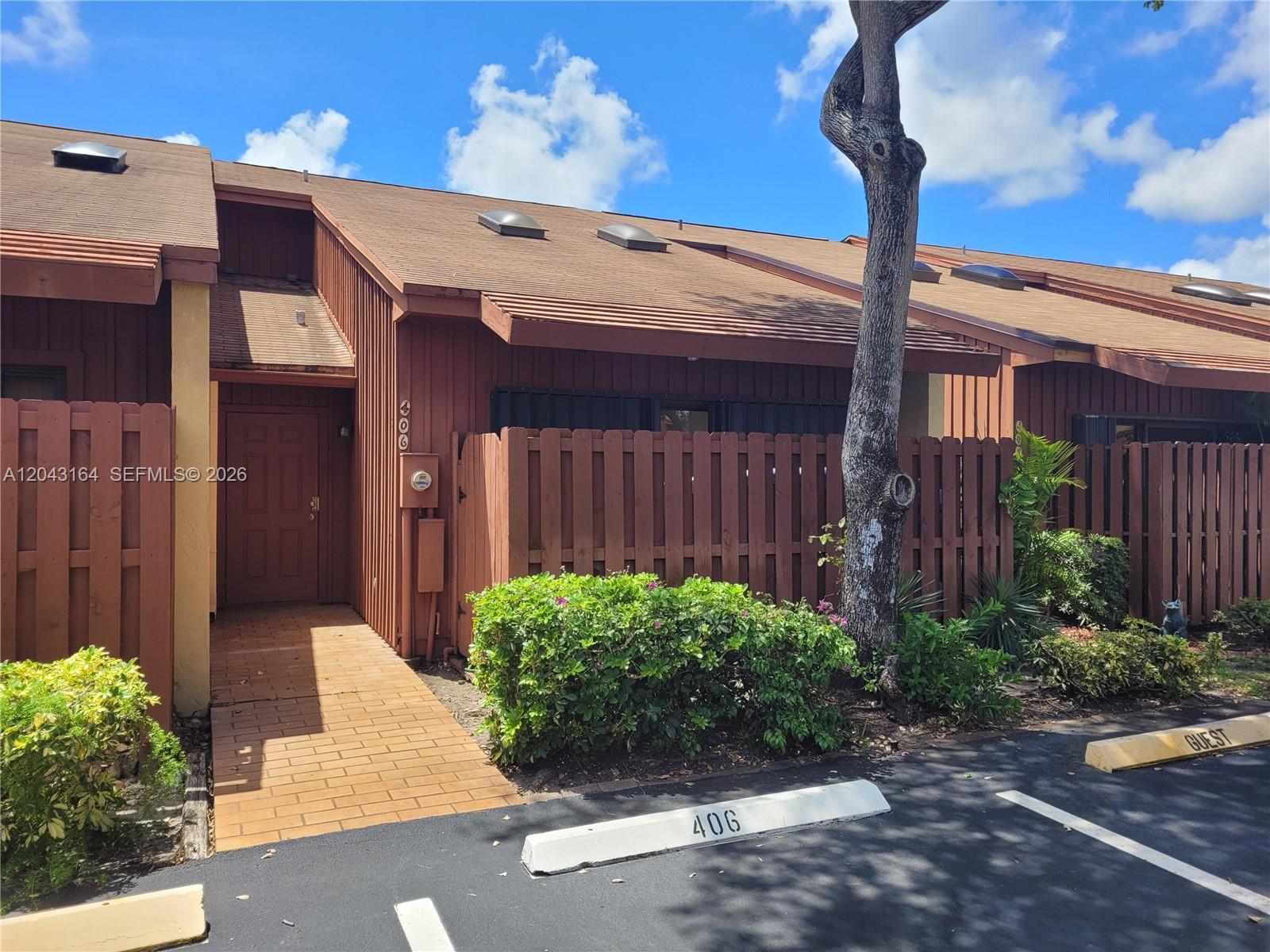 A brown wood-sided townhouse features a brick walkway, a private fence, and a parking space — 406 SE 14th St, Dania Beach FL 33004, DANIA BEACH, FL