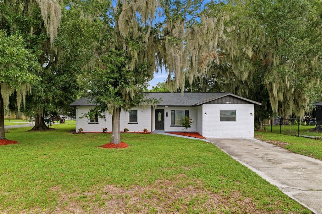 A single-story white brick house with a dark roof sits on a grassy lot — 2419 RIDGEVIEW DRIVE, LAKELAND, FL