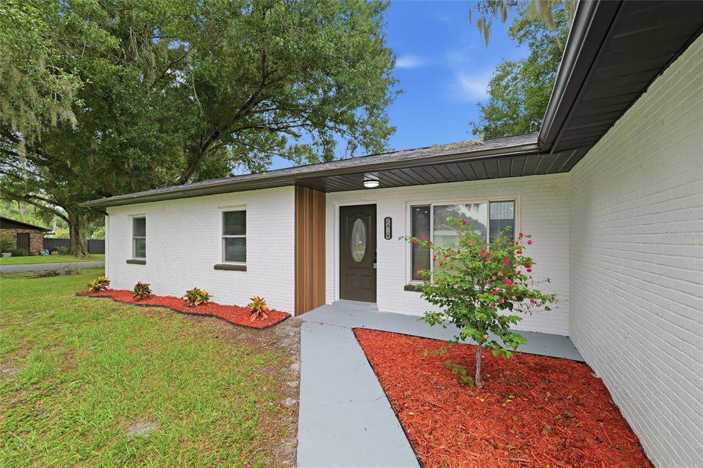 A white brick house exterior features a brown front door, wood accents, and red mulch — 2419 RIDGEVIEW DRIVE, LAKELAND, FL