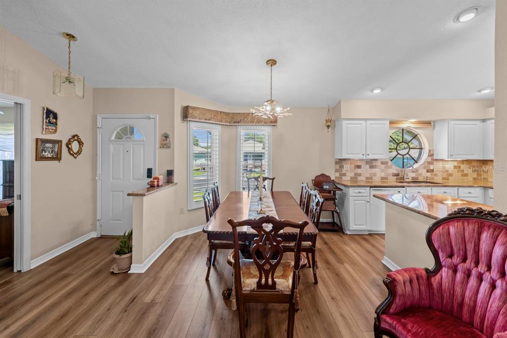 A dining area with wood-look flooring, a long table, and an adjacent kitchen with white cabinets — 6323 SILVER LAKES DRIVE E, LAKELAND, FL