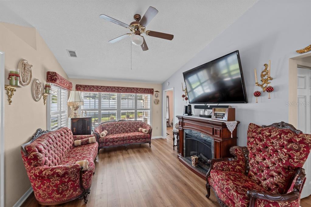 A living room features red patterned furniture, a fireplace with a television, and wood flooring — 6323 SILVER LAKES DRIVE E, LAKELAND, FL