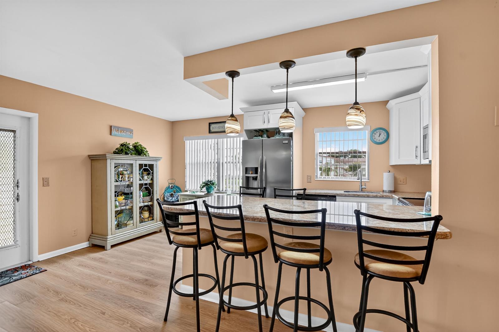 A kitchen with a granite breakfast bar, three stools, stainless steel appliances, and light wood flooring — 351 Fanshaw I, Boca Raton FL 33434, BOCA RATON, FL