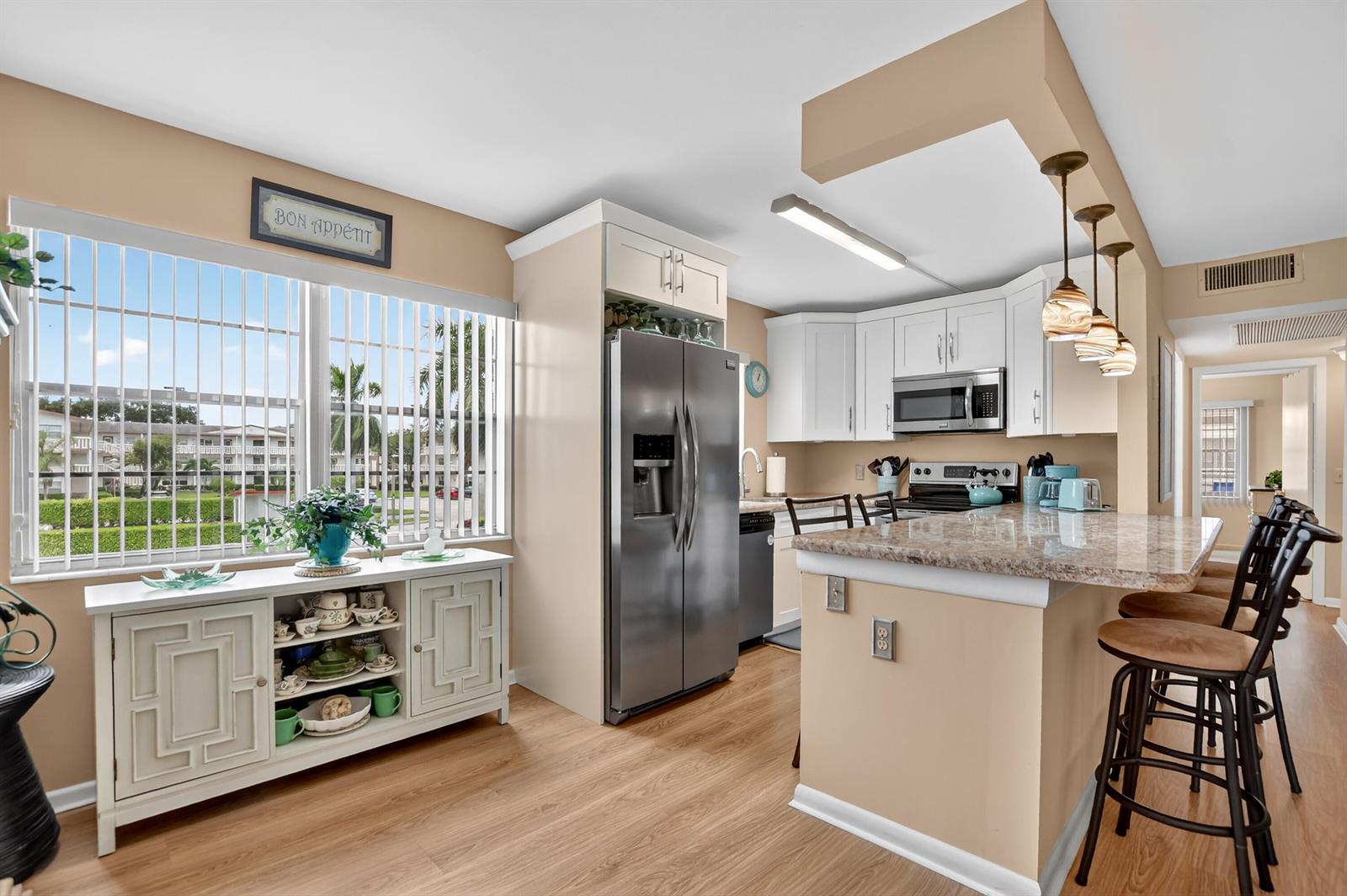 A kitchen features white cabinetry, stainless steel appliances, a granite breakfast bar, and wood flooring — 351 Fanshaw I, Boca Raton FL 33434, BOCA RATON, FL