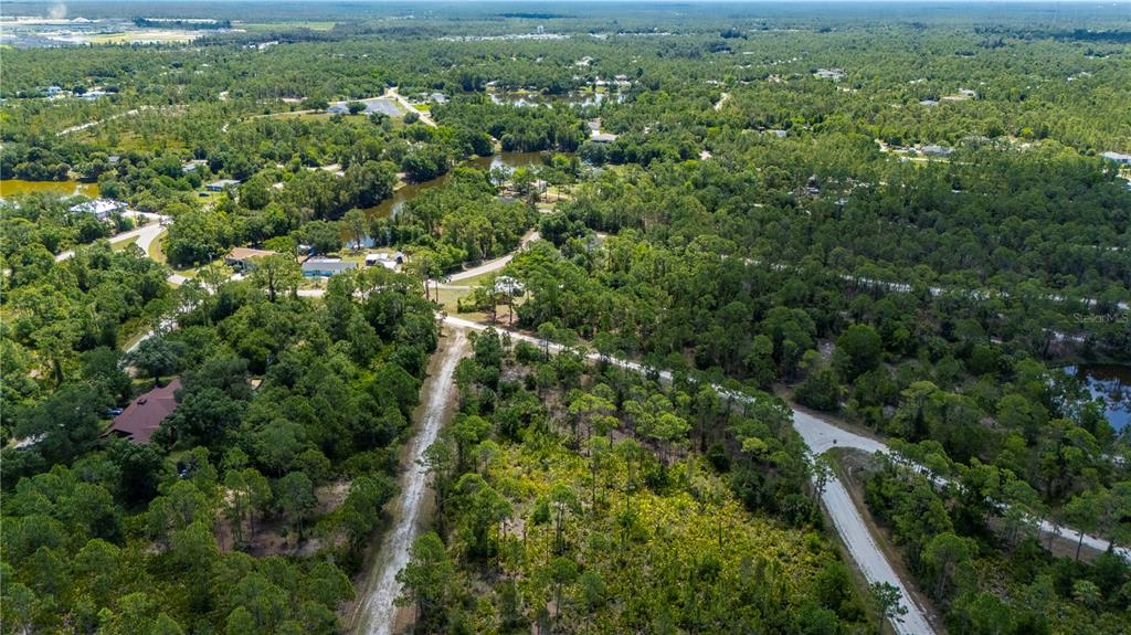 An aerial view shows a dirt road winding through a wooded area with scattered houses — 27115 LACOQUINA DRIVE, PUNTA GORDA, FL