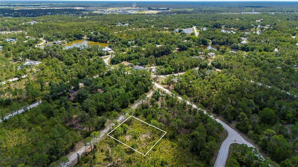 An aerial view shows a rectangular plot of land outlined in white amidst wooded surroundings — 27115 LACOQUINA DRIVE, PUNTA GORDA, FL