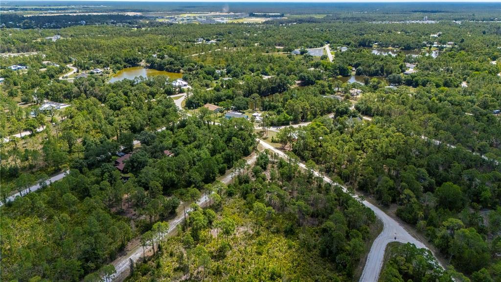 An aerial view shows a wooded residential area with dirt roads and several small ponds — 27115 LACOQUINA DRIVE, PUNTA GORDA, FL
