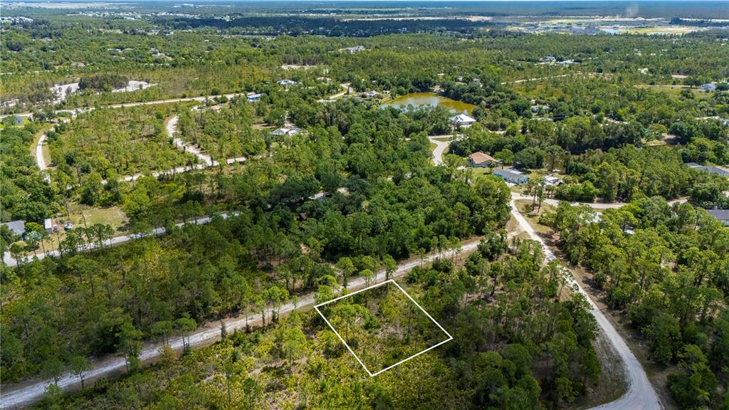 An aerial view shows a vacant, wooded lot outlined in white near a dirt road — 27115 LACOQUINA DRIVE, PUNTA GORDA, FL
