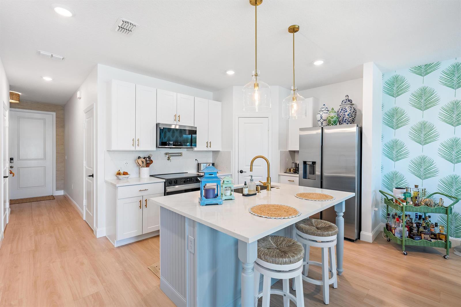 A kitchen features white cabinetry, a light blue island, stainless steel appliances, and palm-patterned wallpaper — 327 SE Halifax Lane, Stuart FL 34994, STUART, FL