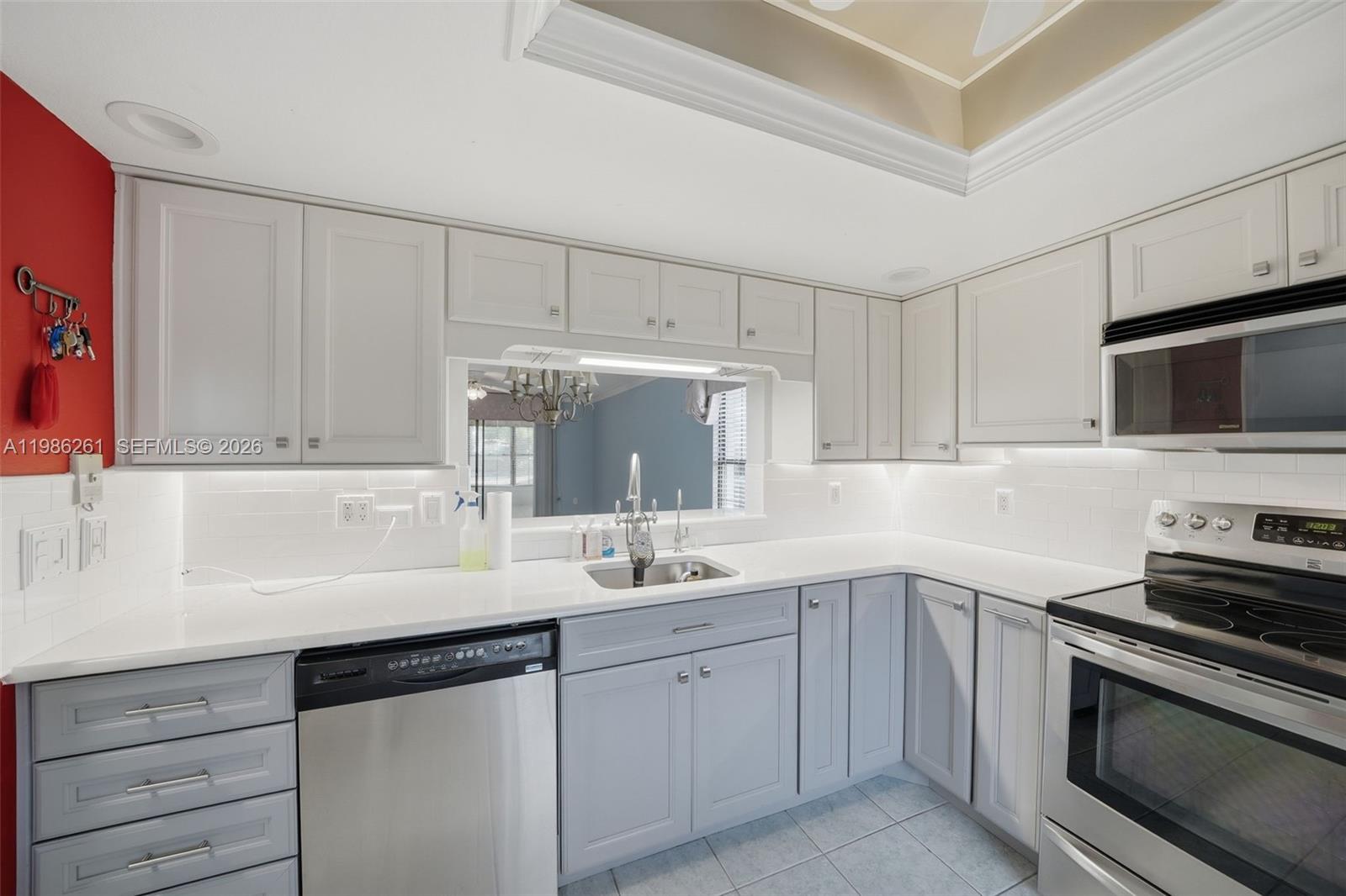 A kitchen features light gray cabinets, white countertops, stainless steel appliances, and a pass-through window — 2130 ELM ST # 401, Clearwater FL 34698, CLEARWATER, FL