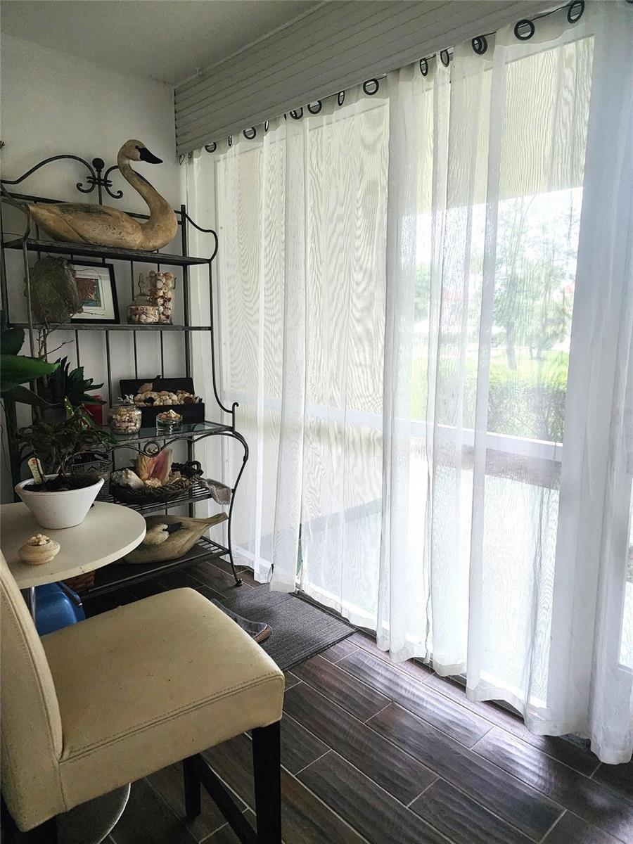 A sunroom features a metal shelving unit, a small table, a chair, and sheer curtains — 804 SE 7th Street # 101, Deerfield Beach FL 33441, DEERFIELD BEACH, FL