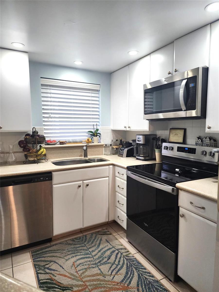 A kitchen features white cabinets, stainless steel appliances, a window, and a patterned floor rug — 804 SE 7th Street # 101, Deerfield Beach FL 33441, DEERFIELD BEACH, FL