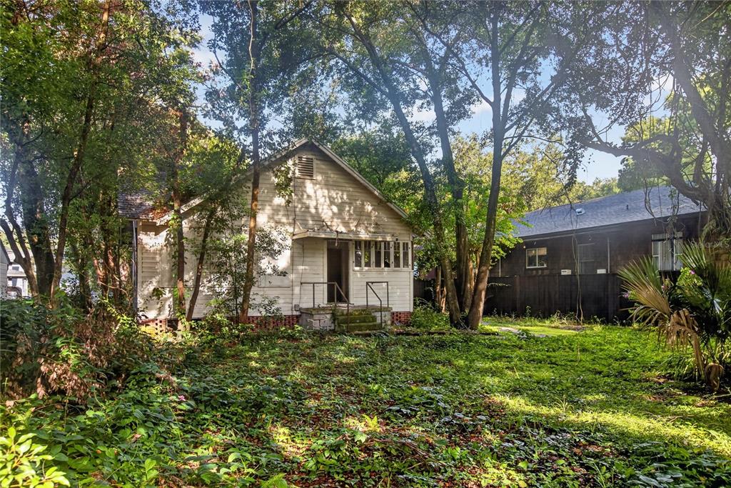 A weathered white house with a front porch sits in a yard overgrown with vegetation — 27 N MILLS AVENUE, ORLANDO, FL