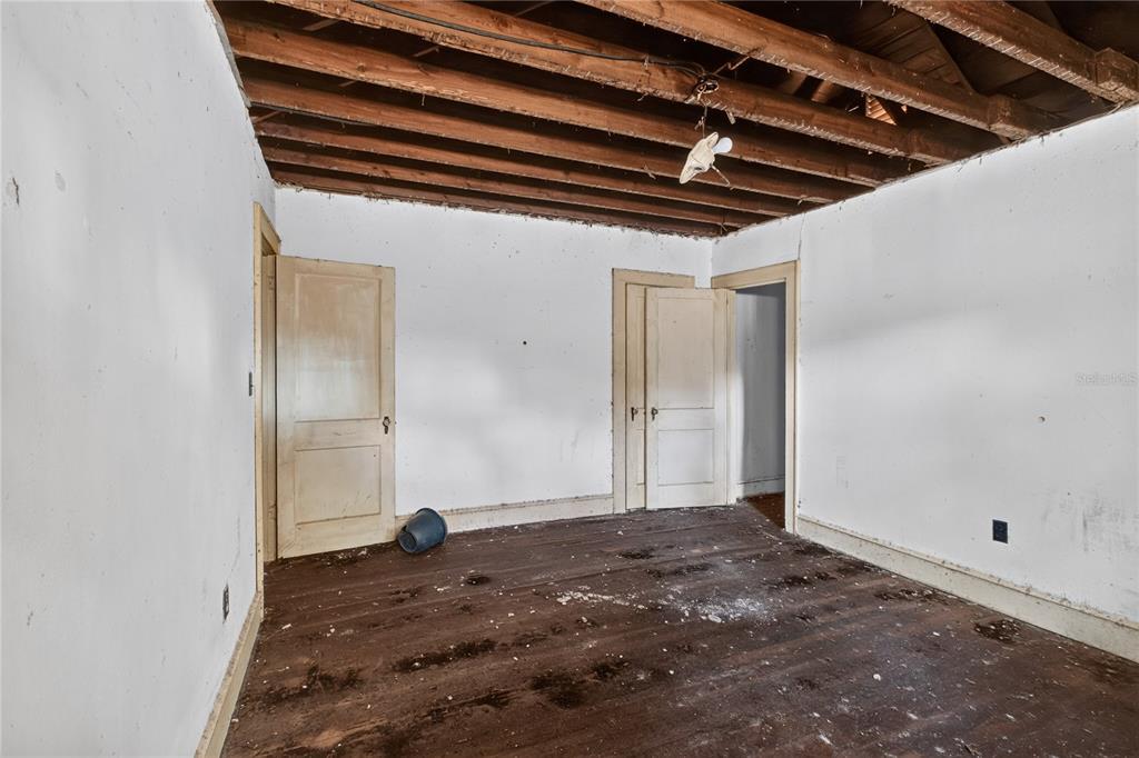 An unfinished room features exposed ceiling joists, white walls, wooden doors, and dark wood flooring — 27 N MILLS AVENUE, ORLANDO, FL