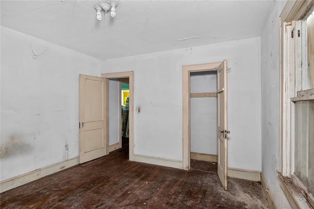An empty bedroom with white walls, wood flooring, two open doorways, and a window — 27 N MILLS AVENUE, ORLANDO, FL