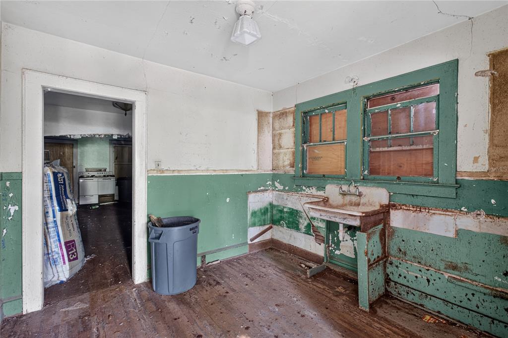 A dilapidated kitchen features a vintage wall-mounted sink, peeling green paint, and exposed wood flooring — 27 N MILLS AVENUE, ORLANDO, FL