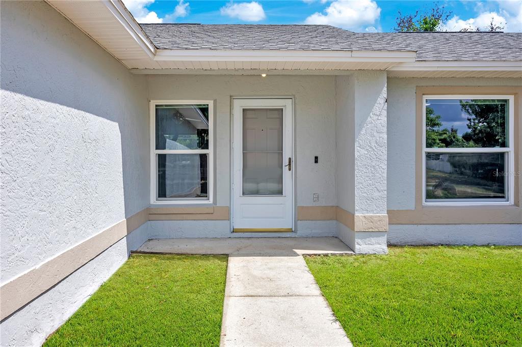 The exterior of a house features a white front door, two windows, and a walkway — 10652 CRESCENDO LOOP, CLERMONT, FL