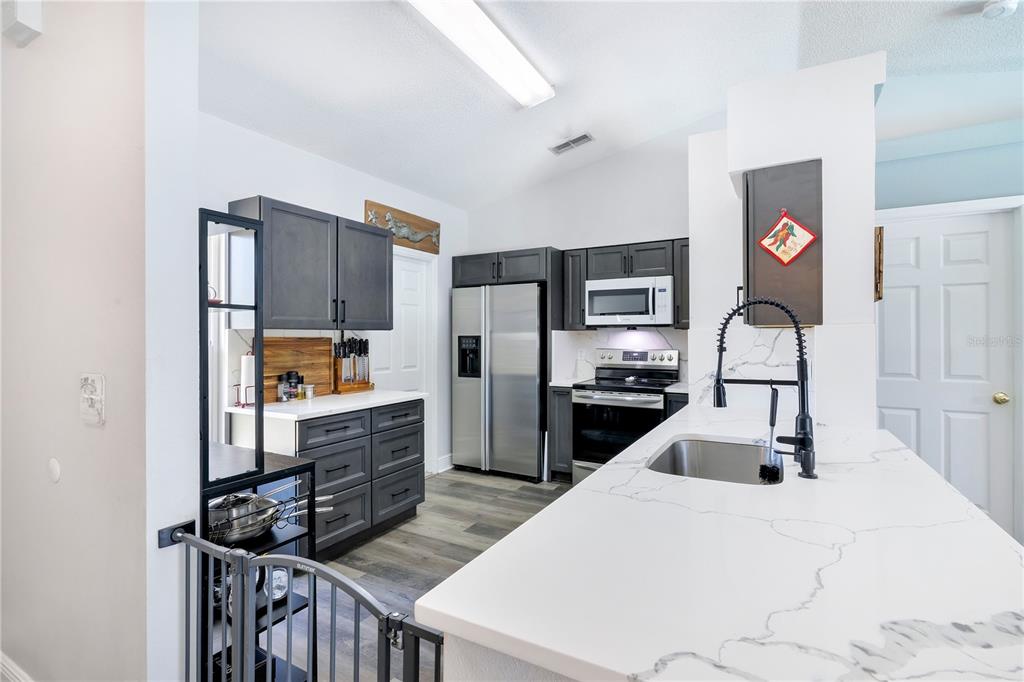 A kitchen features dark gray cabinets, stainless steel appliances, and a white quartz countertop — 10652 CRESCENDO LOOP, CLERMONT, FL