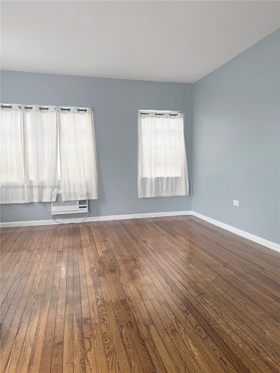 An empty room features light blue walls, hardwood floors, and two windows with white curtains — 1730 Marseille Dr # 4, Miami Beach FL 33141, MIAMI BEACH, FL