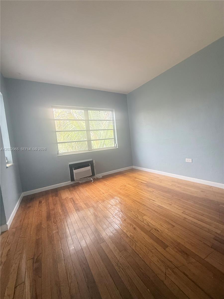 An empty room features light blue walls, hardwood flooring, and a window air conditioning unit — 1730 Marseille Dr # 4, Miami Beach FL 33141, MIAMI BEACH, FL