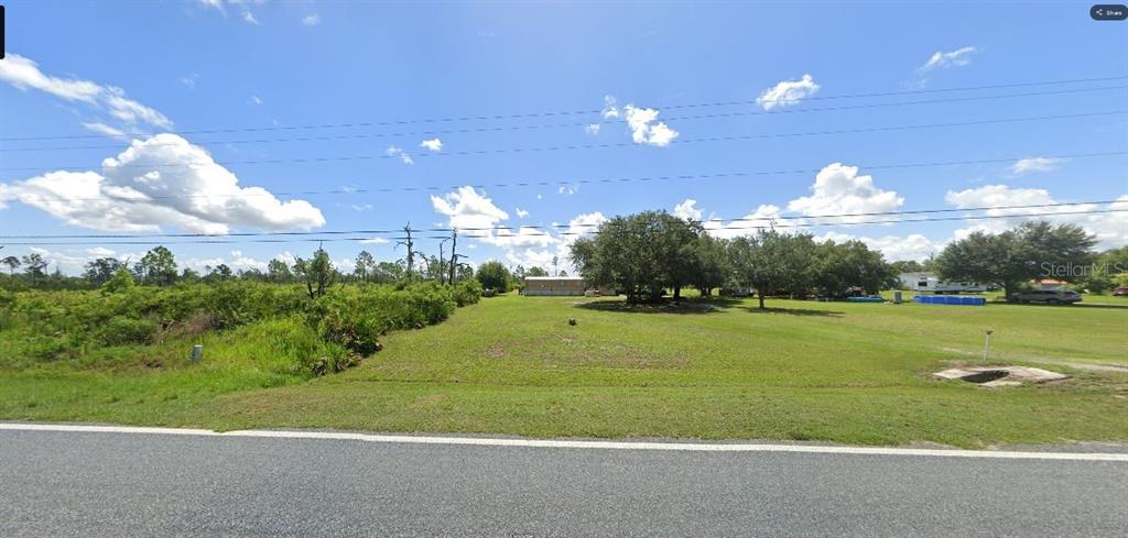 A grassy, vacant lot sits along a paved road with trees and a distant house — TIGER LAKE ROAD, LAKE WALES, FL