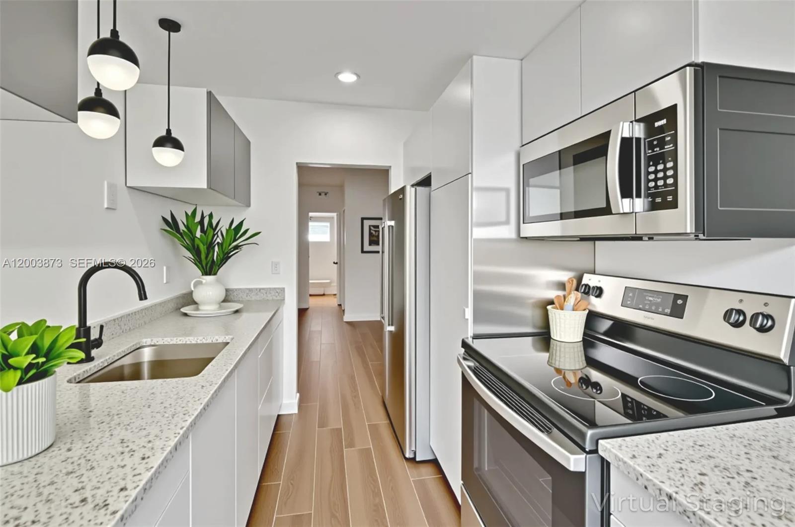 A modern galley kitchen features white cabinets, granite countertops, stainless steel appliances, and pendant lighting — 1334 Euclid Ave # 8, Miami Beach FL 33139, MIAMI BEACH, FL