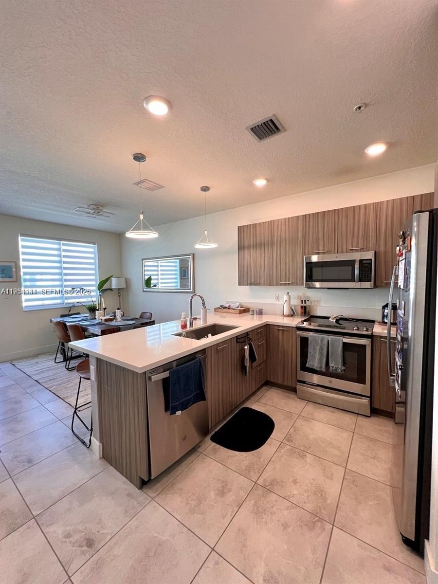 A modern kitchen features wood-tone cabinets, stainless steel appliances, and a white quartz island — 6420 NW 102nd Path # 304, Doral FL 33178, DORAL, FL