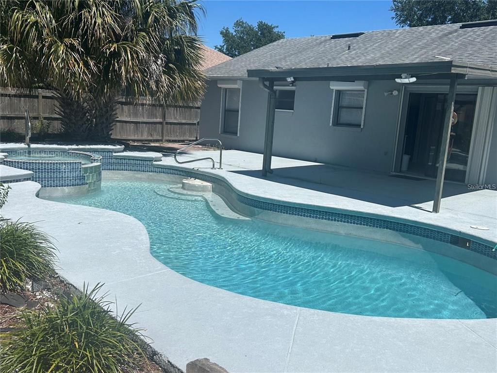 A backyard features a swimming pool with an attached spa and a covered patio area — 613 BAYPORT DRIVE, KISSIMMEE, FL