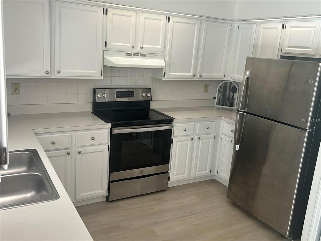 A kitchen features white cabinets, stainless steel appliances, and light-colored countertops — 613 BAYPORT DRIVE, KISSIMMEE, FL