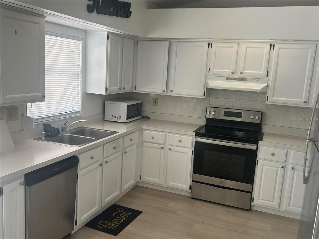 A kitchen features white cabinets, stainless steel appliances, light countertops, and light wood-look flooring — 613 BAYPORT DRIVE, KISSIMMEE, FL