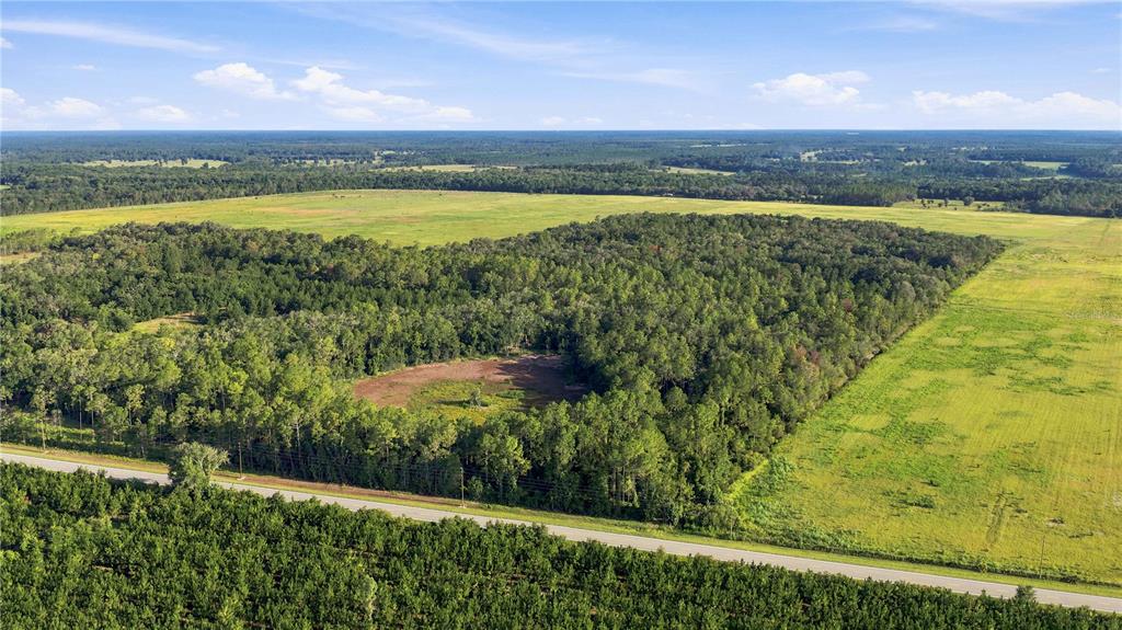 An aerial view shows a rural landscape with a road bordering a wooded area and fields — 0 E HIGHWAY 318, CITRA, FL