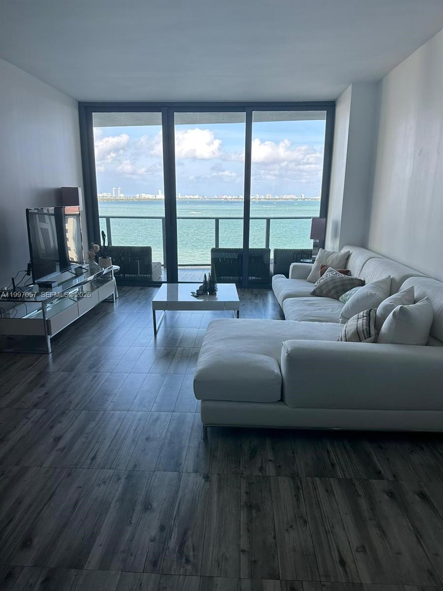 A living room with a white sectional sofa, glass coffee table, and floor-to-ceiling balcony windows — 460 NE 28th St # 705, Miami FL 33137, MIAMI, FL