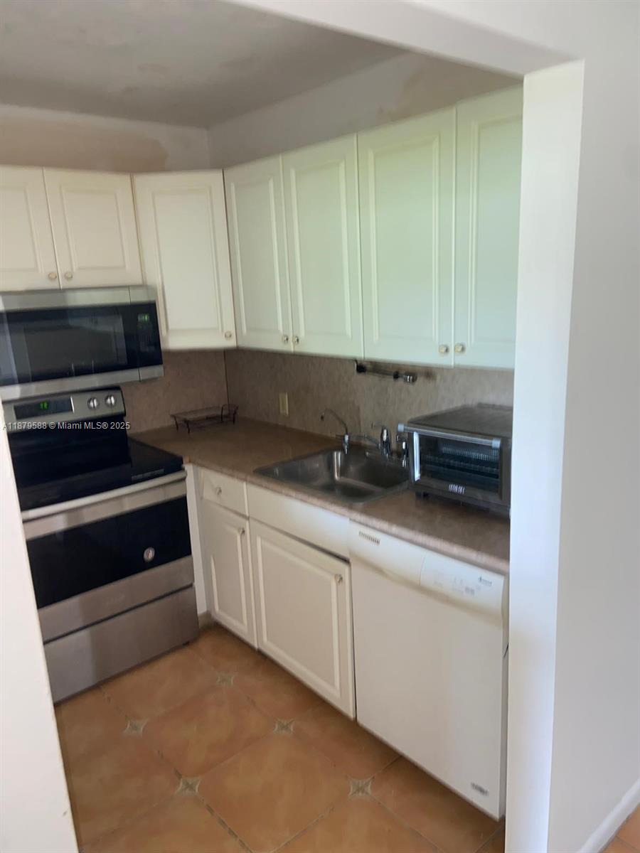 A kitchen features white cabinets, stainless steel appliances, a double sink, and tiled flooring — 8 Fanshaw A # 8, Boca Raton FL 33434, BOCA RATON, FL