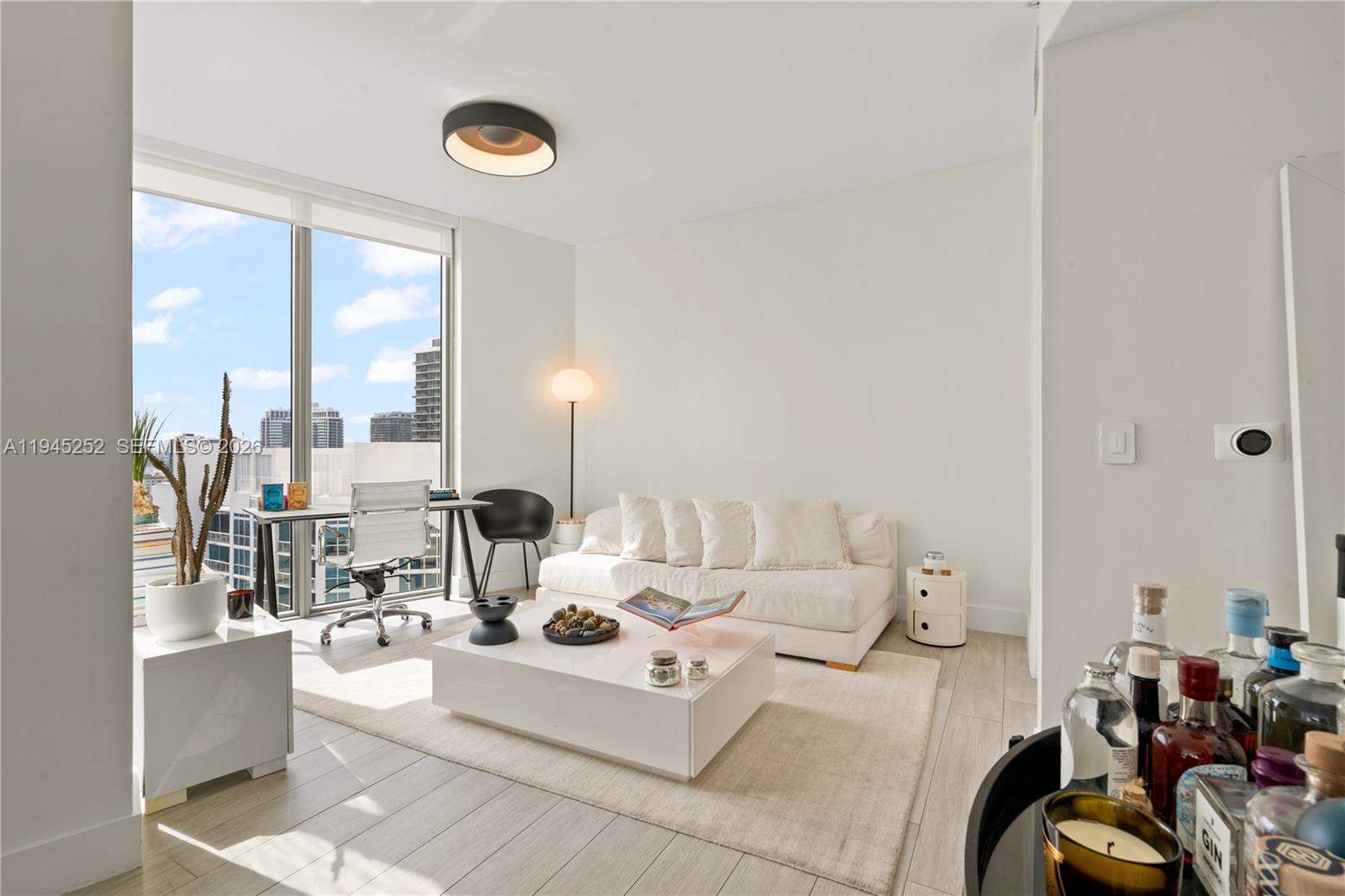 A bright living room features a white sofa, coffee table, desk, and floor-to-ceiling windows — 2900 NE 7th Ave # 2309, Miami FL 33137, MIAMI, FL