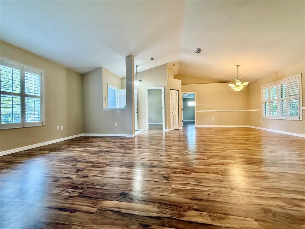 A spacious living area features wood-look flooring, vaulted ceilings, and white plantation shutters — 8032 SW 51ST LANE, GAINESVILLE, FL