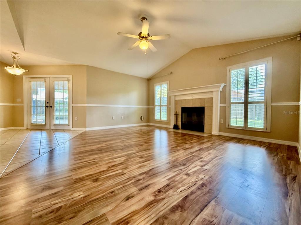 A living room features wood-look flooring, a vaulted ceiling with a fan, and a fireplace — 8032 SW 51ST LANE, GAINESVILLE, FL