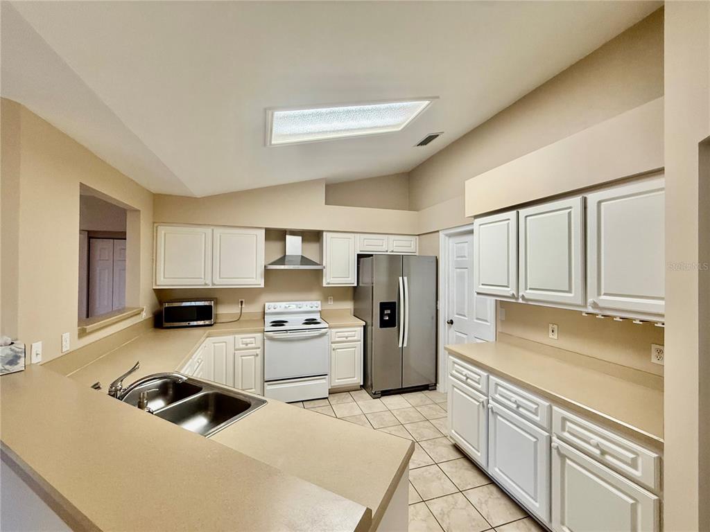 A kitchen features white cabinets, stainless steel appliances, tan countertops, and tile flooring — 8032 SW 51ST LANE, GAINESVILLE, FL