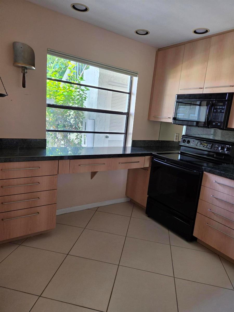 A kitchen features light wood cabinets, dark countertops, a black stove, and a window view — 21500 Cypress Hammock Drive # 38e, Boca Raton FL 33428, BOCA RATON, FL