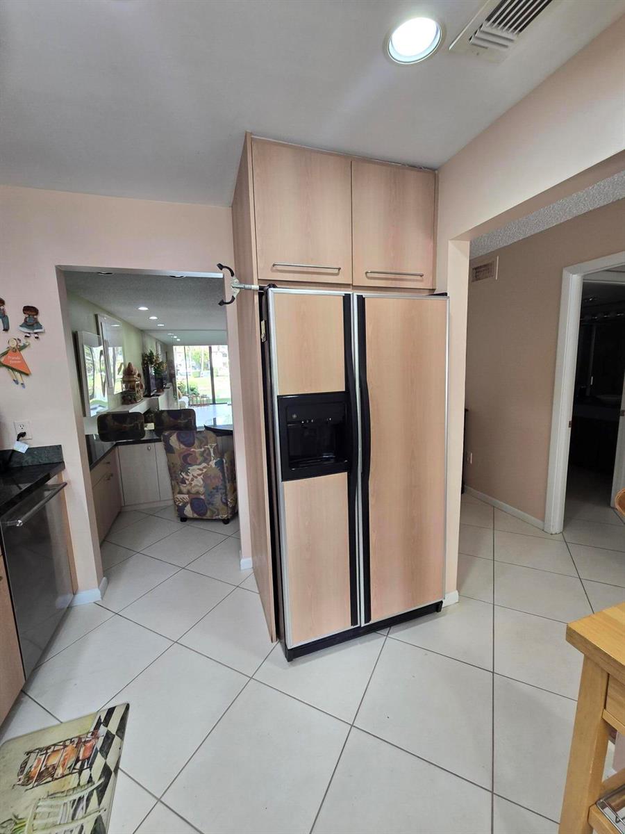 A kitchen features a light wood-paneled refrigerator with overhead cabinets and light-colored floor tiles — 21500 Cypress Hammock Drive # 38e, Boca Raton FL 33428, BOCA RATON, FL