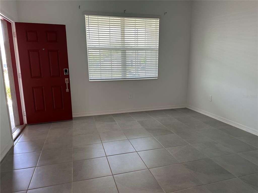 An empty room features gray tile flooring, a red front door, and a window with blinds — 4162 BABBLING BROOK WAY UNIT B, KISSIMMEE, FL