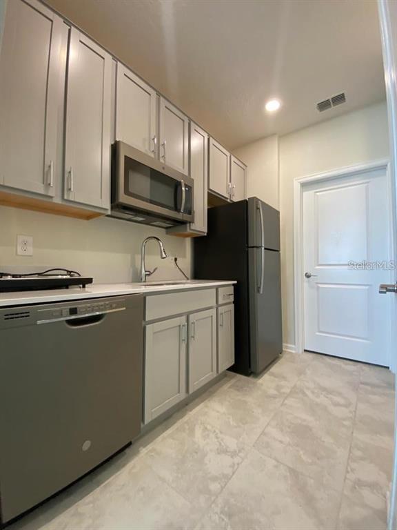 A kitchen features gray cabinets, stainless steel appliances, white countertops, and light-colored tile flooring — 4162 BABBLING BROOK WAY UNIT B, KISSIMMEE, FL