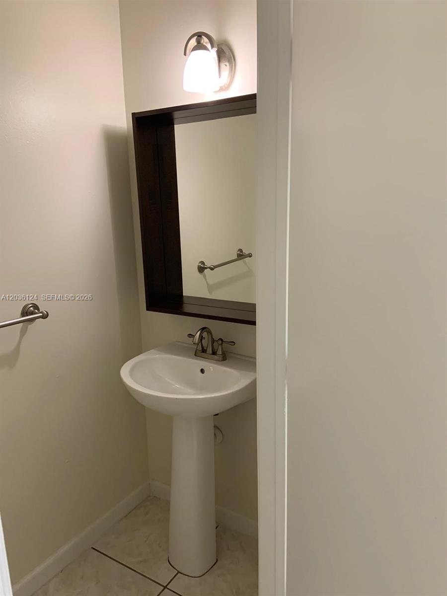 A small bathroom features a white pedestal sink, a dark-framed mirror, and a wall-mounted light — WESTON, FL