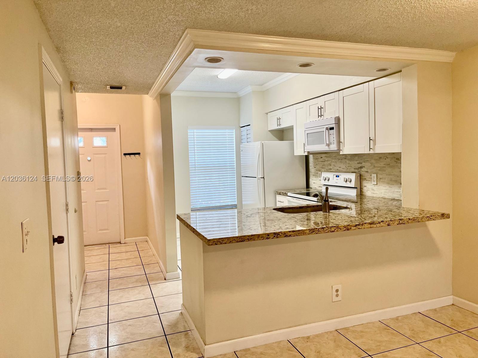 A kitchen features white cabinets, granite countertops, and a breakfast bar overlooking a tiled floor — WESTON, FL