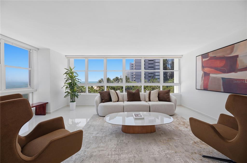 A modern living room features a white sofa, two brown armchairs, and floor-to-ceiling windows — 1503 ASHFORD AVENUE UNIT 3C, SAN JUAN, PR