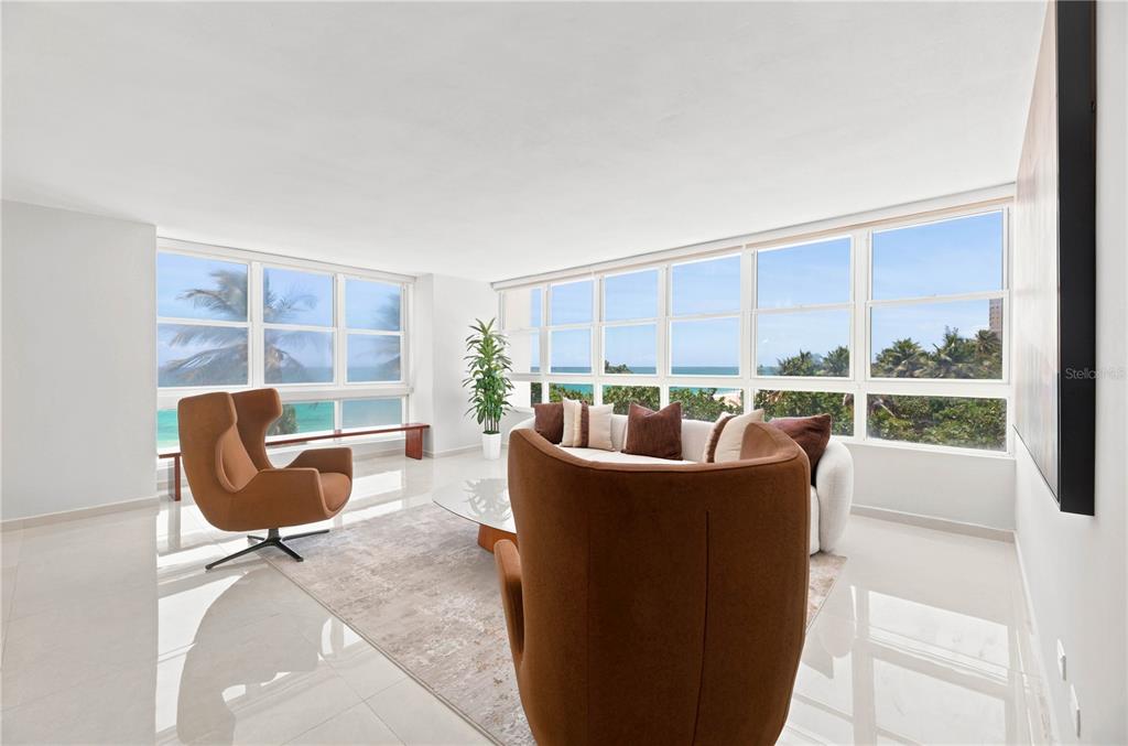 A bright living room features white tile floors, modern furniture, and large windows overlooking the ocean — 1503 ASHFORD AVENUE UNIT 3C, SAN JUAN, PR
