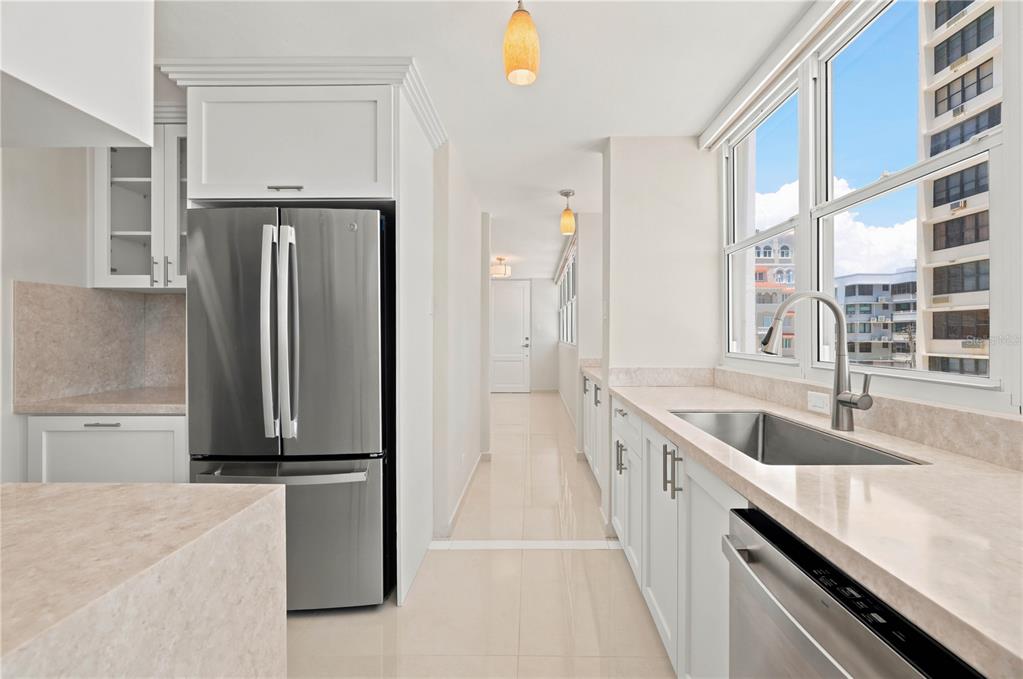 A modern kitchen features white cabinetry, stainless steel appliances, and a view of nearby buildings — 1503 ASHFORD AVENUE UNIT 3C, SAN JUAN, PR