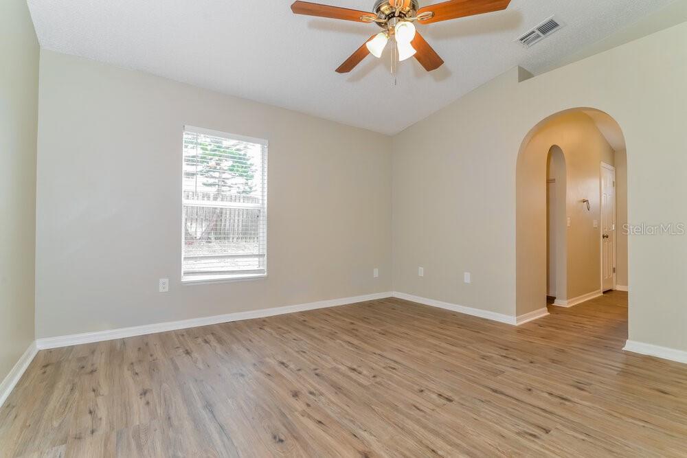An empty bedroom features light-colored walls, wood-look flooring, a ceiling fan, and an arched doorway — 1064 REMINGTON AVENUE, EUSTIS, FL