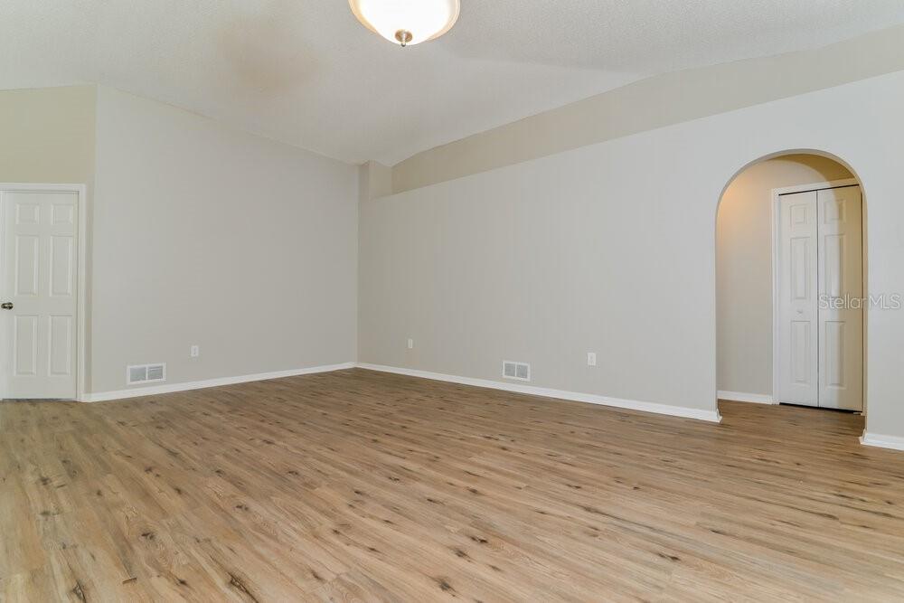 An empty room features light wood-look flooring, neutral walls, and an arched doorway — 1064 REMINGTON AVENUE, EUSTIS, FL