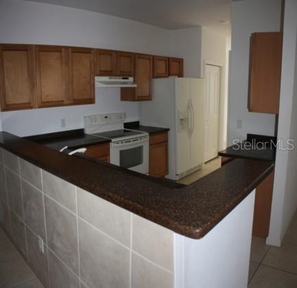 A kitchen features light wood cabinets, dark countertops, a white stove, and a tiled breakfast bar — 2935 NE 7TH STREET UNIT 207, OCALA, FL