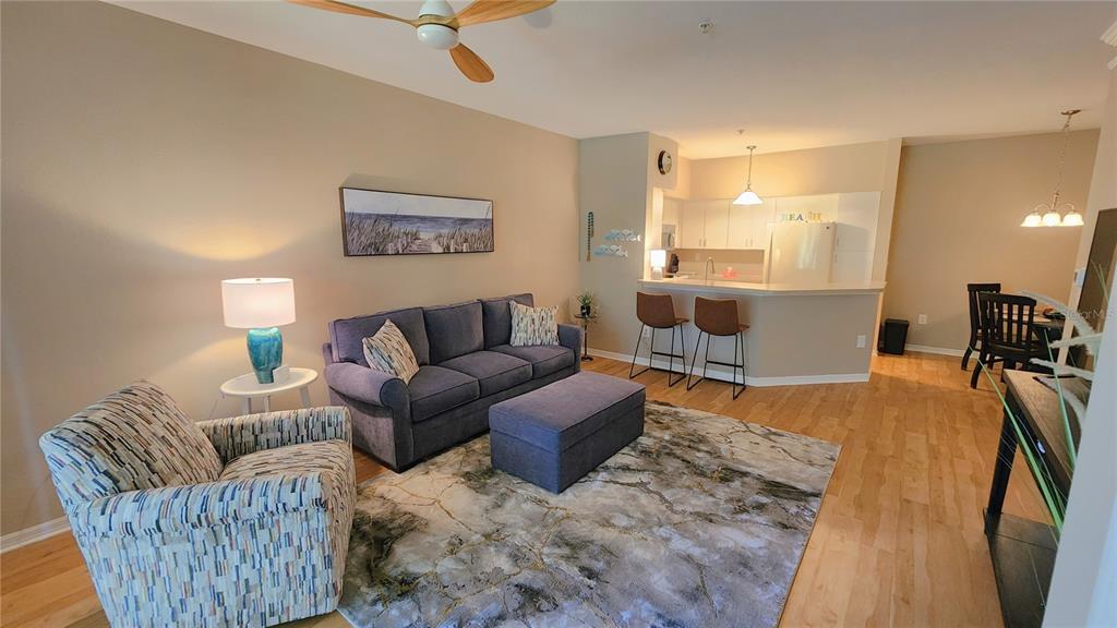 A living room with a blue sofa, patterned armchair, and an open kitchen with bar seating — 4106 CENTRAL SARASOTA PARKWAY UNIT 1018, SARASOTA, FL