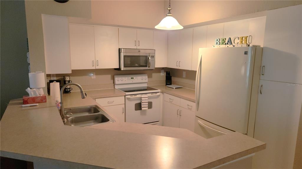 A kitchen features white cabinets, a stainless steel microwave, a white stove, and beige countertops — 4106 CENTRAL SARASOTA PARKWAY UNIT 1018, SARASOTA, FL